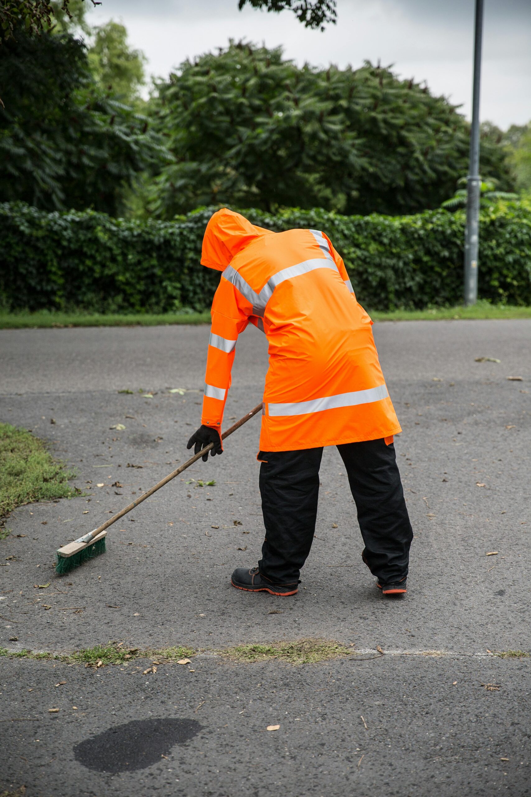 A worker in orange reflective clothing sweeping a street outdoors.
