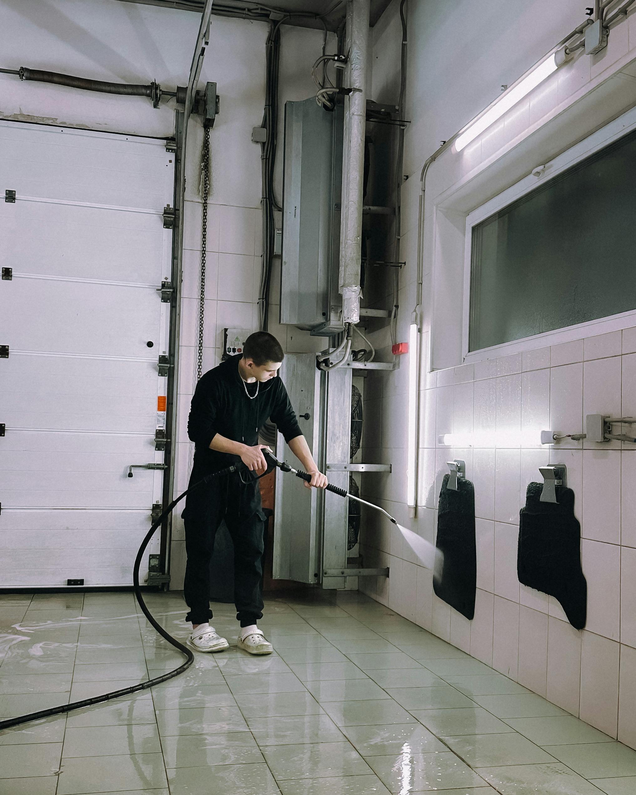 A person uses a power washer in an industrial setting, highlighting safety and cleanliness.